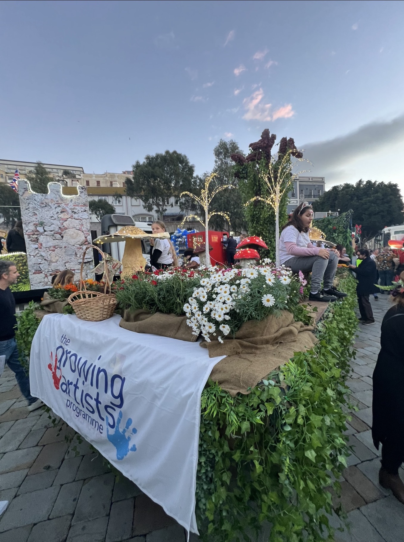 Enchanted Forest themed float with flowers, mushrooms and lit trees at Gibraltar's 2026 Cavalcade, featuring the Growing Artists Programme banner