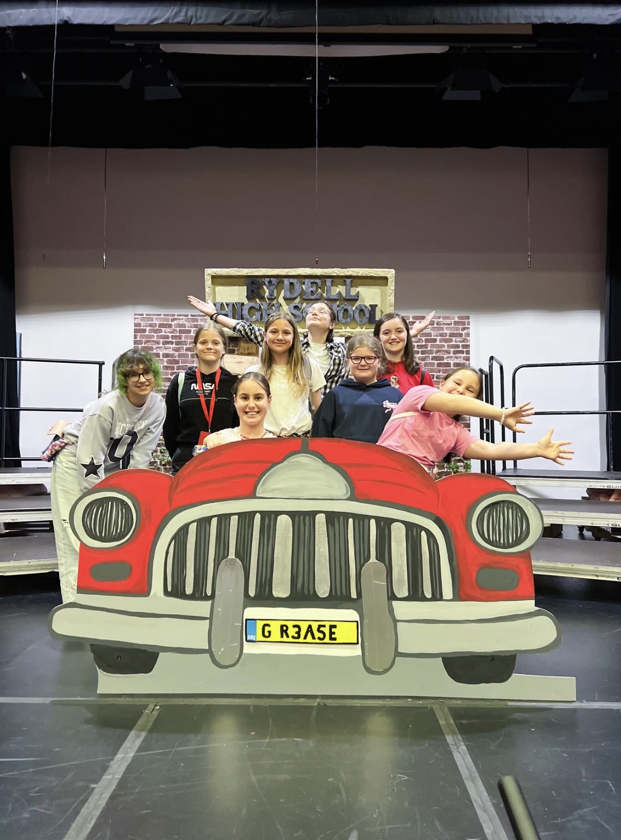 Youth Group members posing with a hand-painted red car set piece for Prior Park School's production of Grease