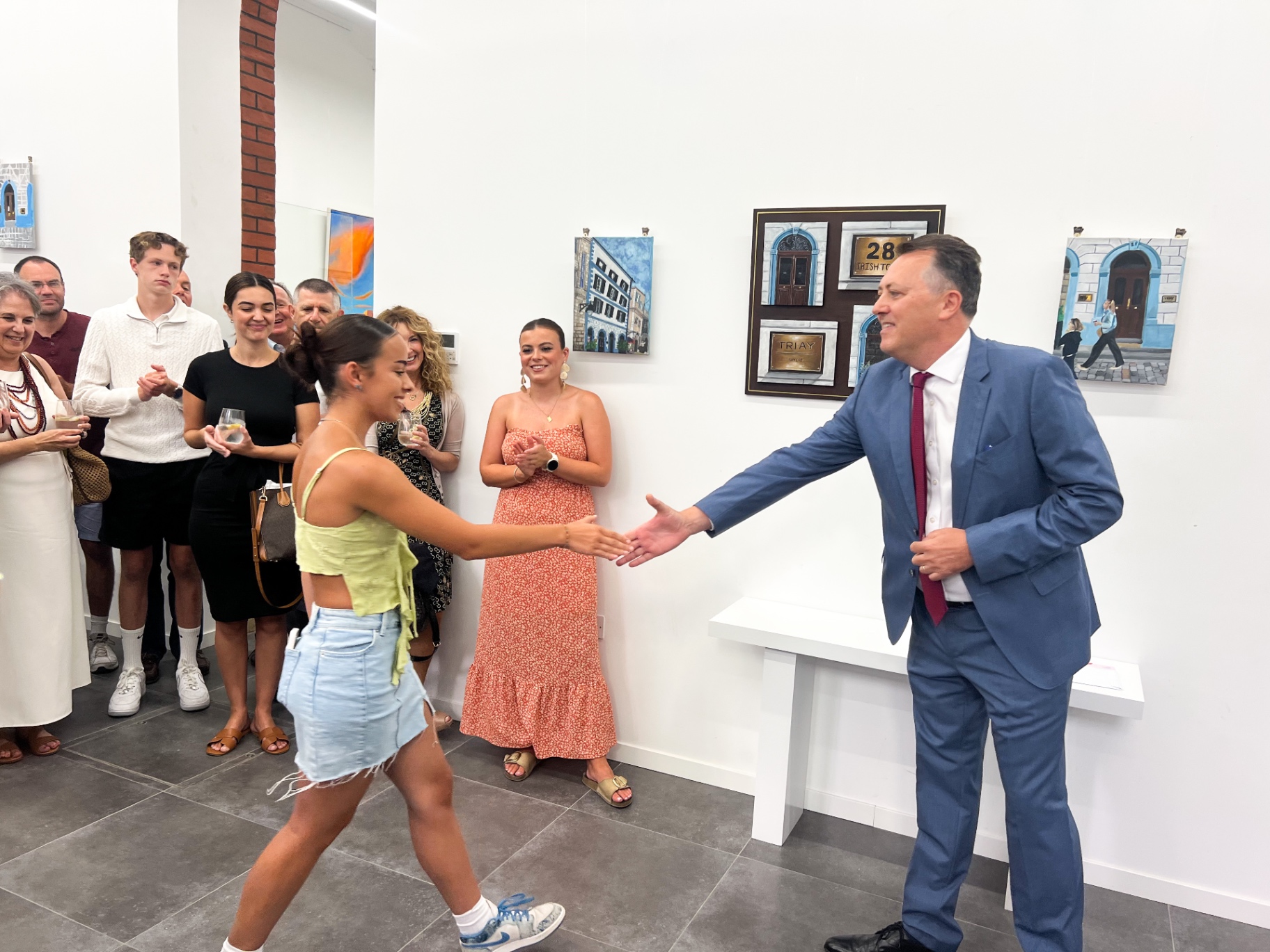 An artist being welcomed at an exhibition opening while guests look on with drinks