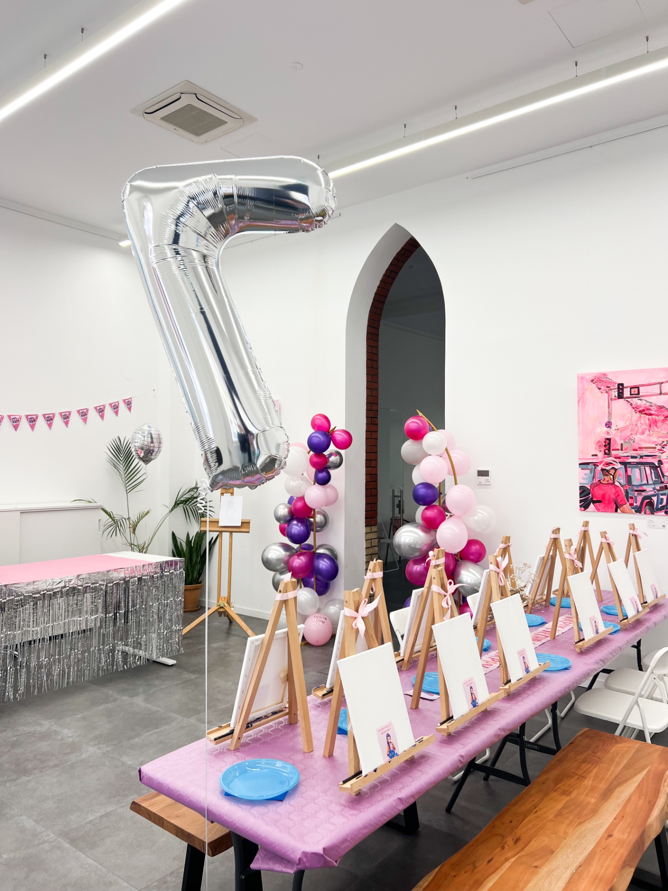 Party room decorated with a giant silver number balloon, balloon garlands and rows of mini easels