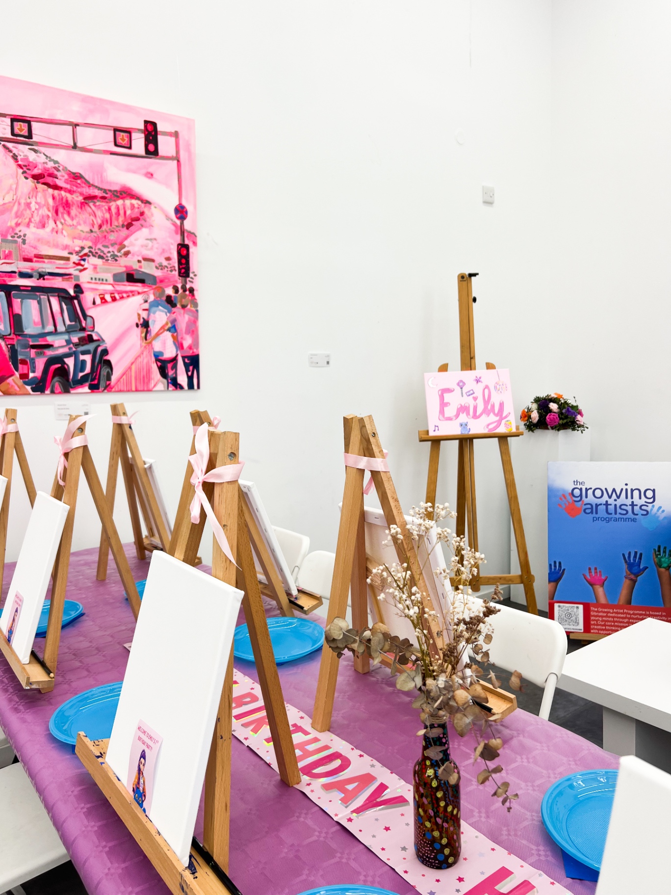 Table of blank canvases on wooden easels tied with pink ribbons, with a personalised painted name sign