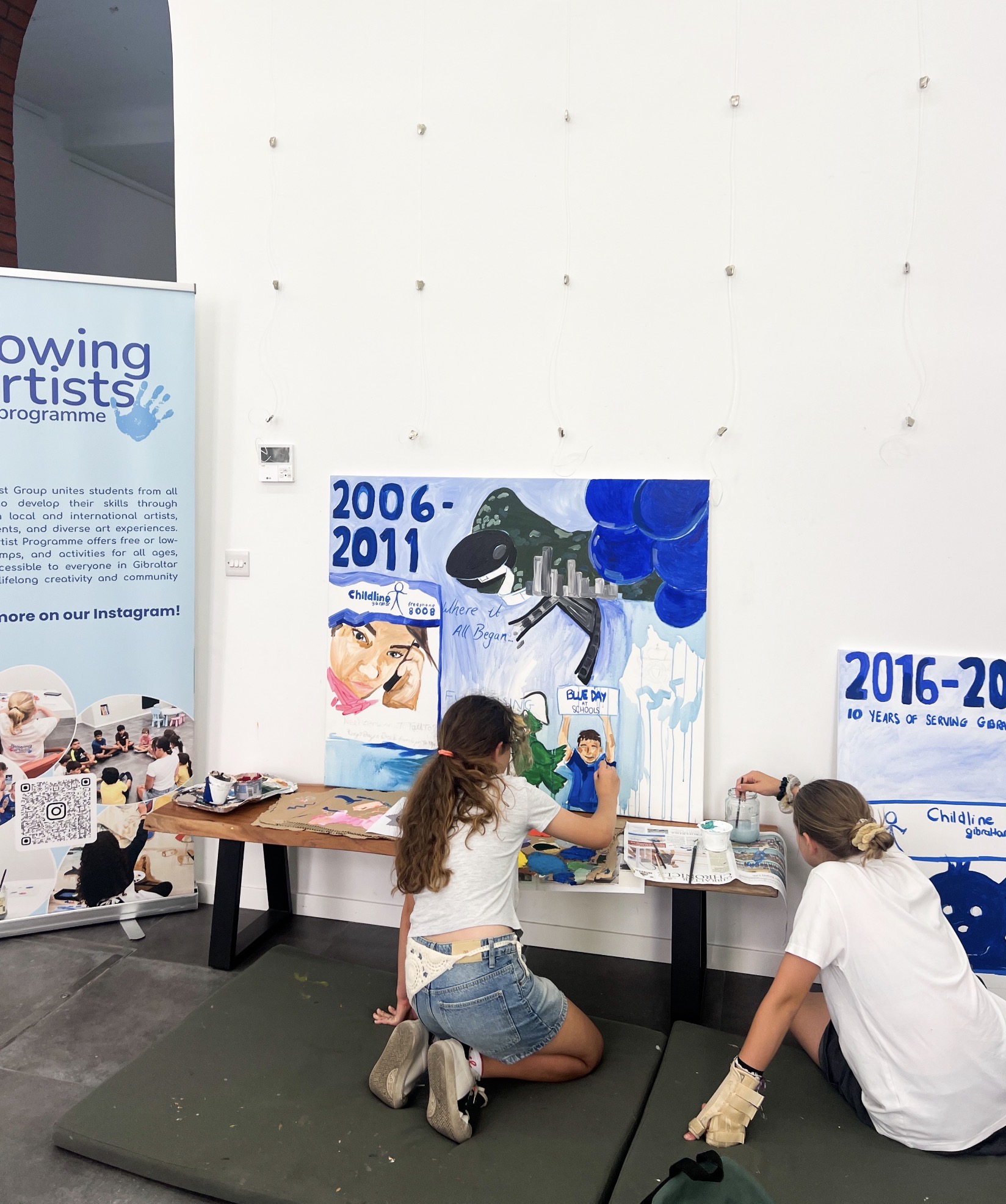 Two Youth Group members painting large canvases marking Childline Gibraltar's 20th anniversary