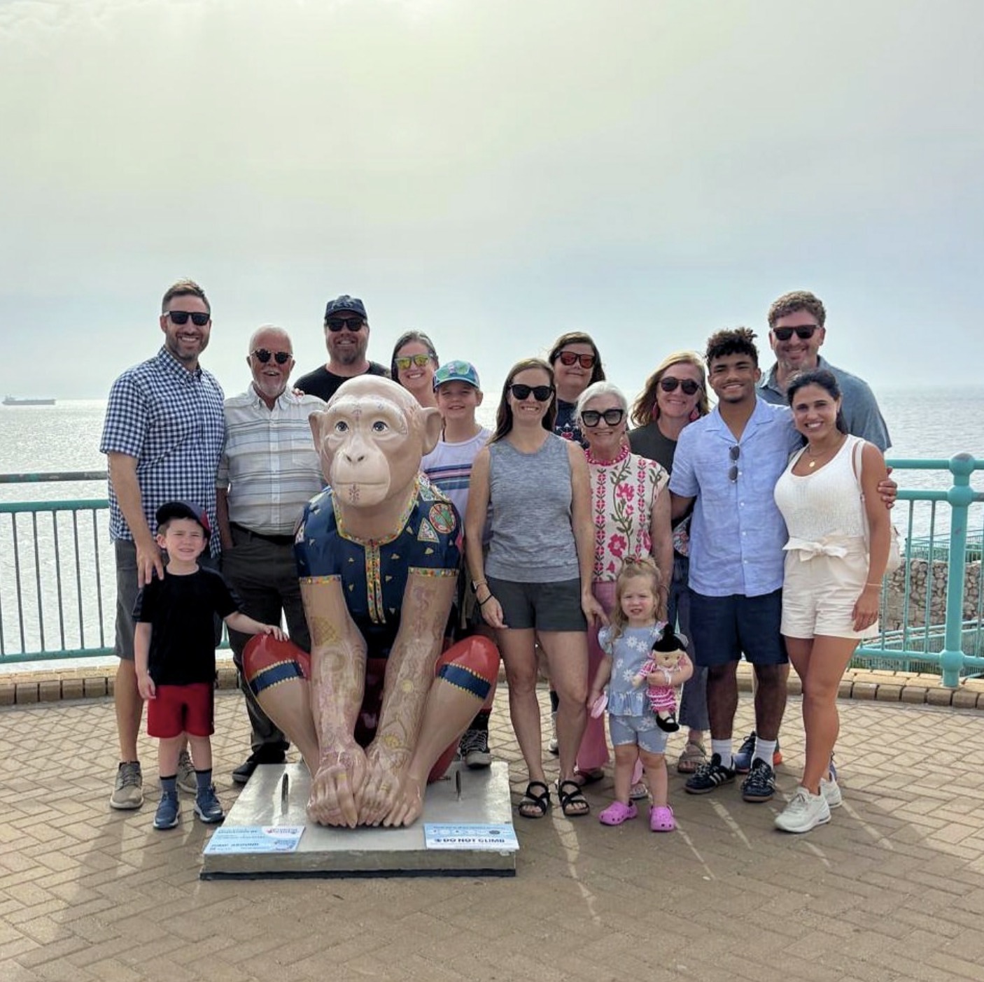 A large family group gathered around a Barbary Macaque sculpture by the sea