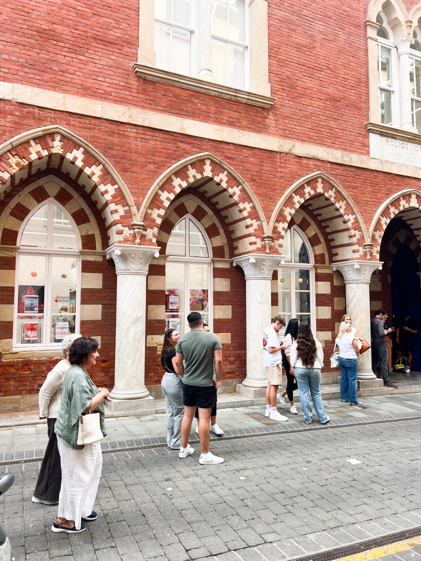 The Old Police Station facade with its red brick arches and crowds outside the hub