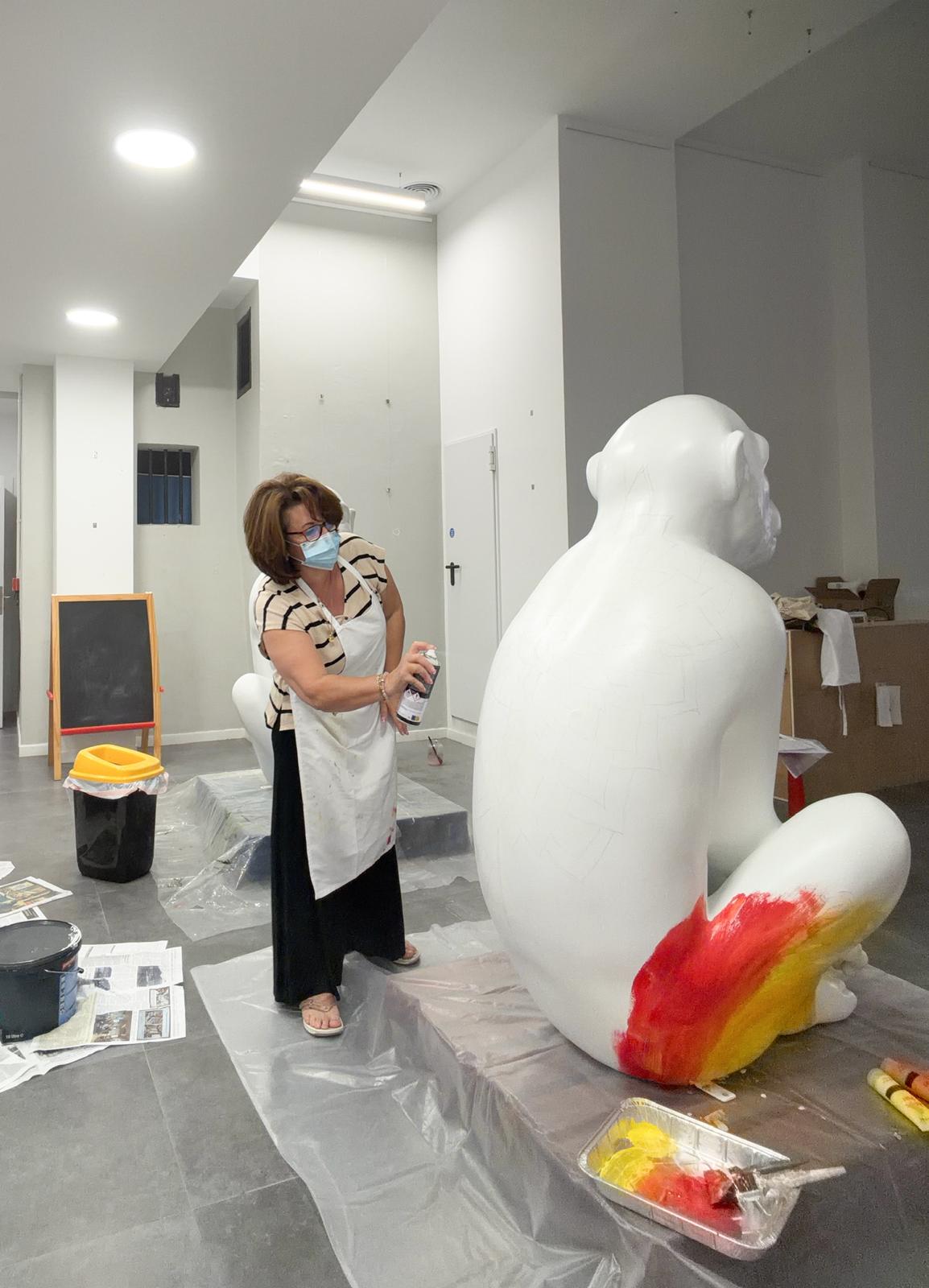 Rose Ann priming the blank white sculpture with the first strokes of red and yellow on the tail