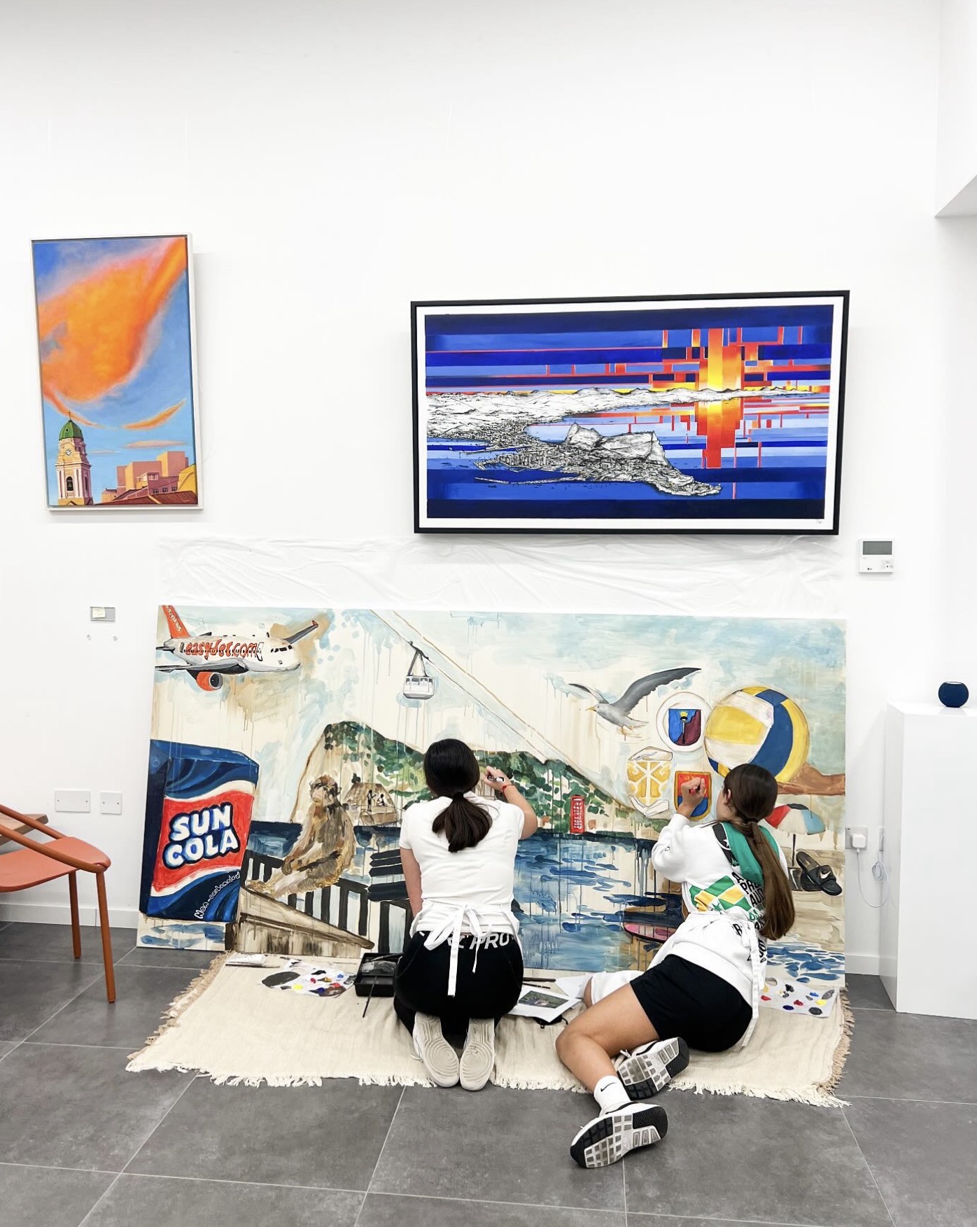 Two young artists painting a large collaborative canvas featuring Gibraltar landmarks