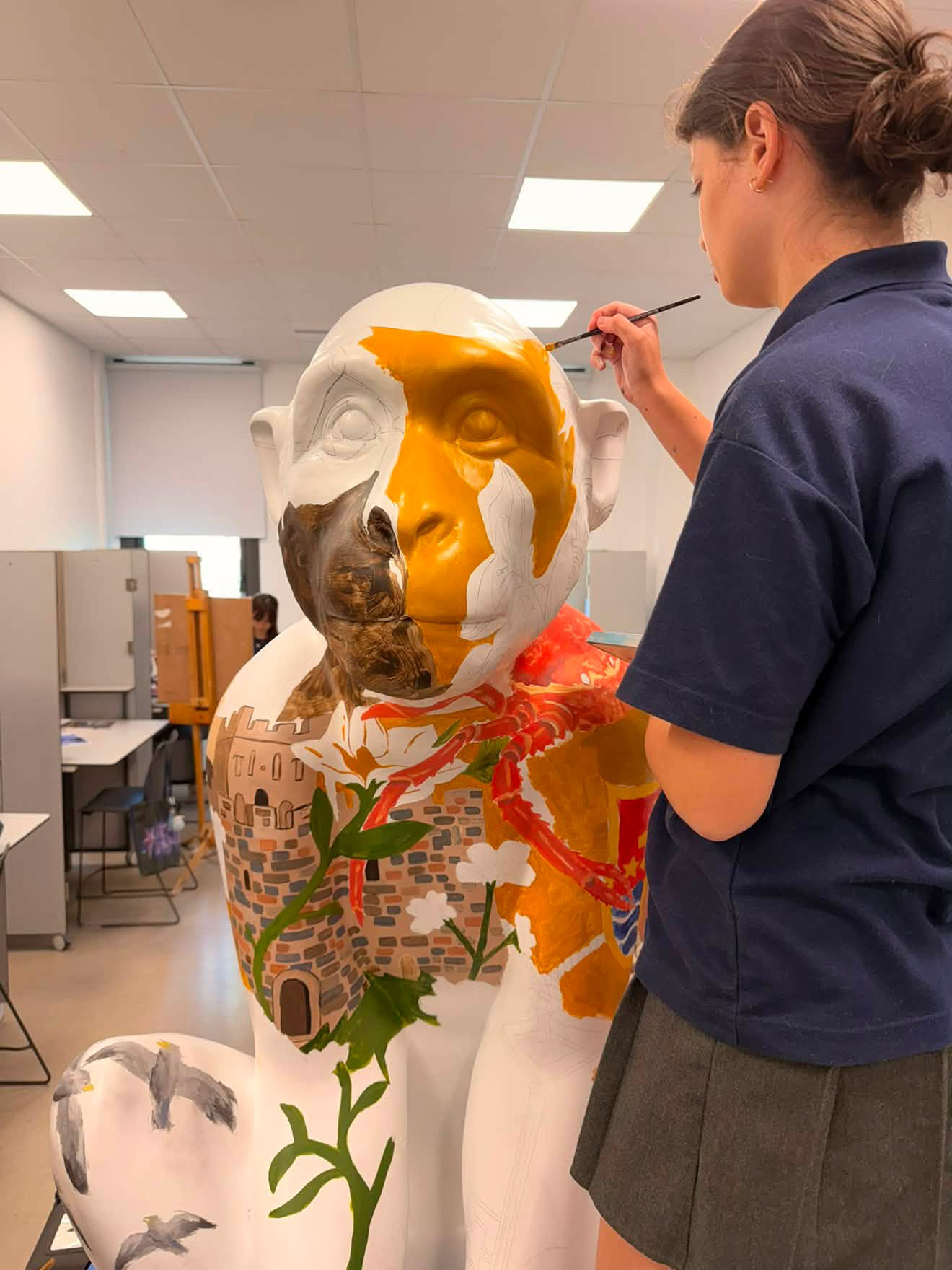 Bayside student painting the first yellow strokes onto Elin's face