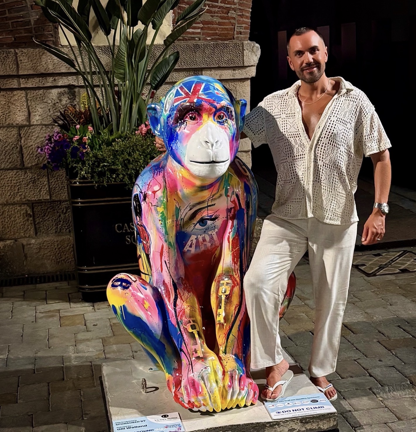 A visitor posing with a colourful Union Jack Barbary Macaque sculpture at night
