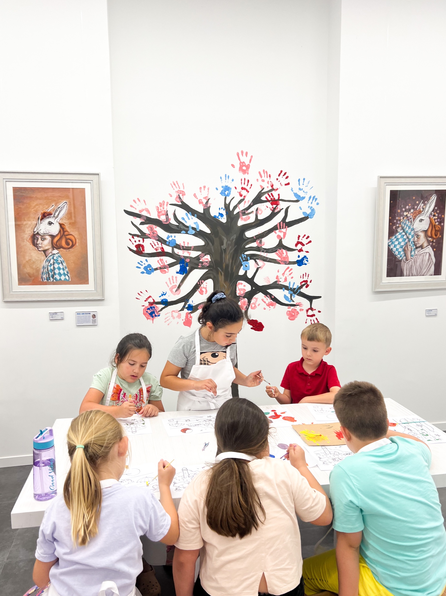 Children from the Art Club class painting around a shared table in the gallery